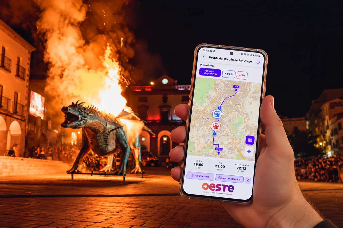 Una persona siguiendo el desfile del Dragón de San Jorge desde el móvil con la app de LiveMap, con el dragón ardiendo en la Plaza Mayor de Cáceres al fondo